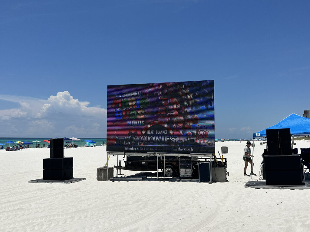 Outdoor movie setup on the beach in Panama City, FL, featuring a large screen and sound equipment for community events by Neves Media.