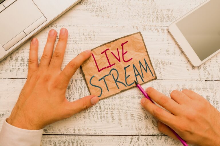 A hand holding a card that says "LIVE STREAM" with a pink pen nearby. Neves Media provides digital solutions in Panama City, FL.